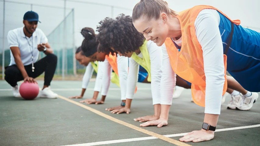 Netball team doing warm-up on court with their coach